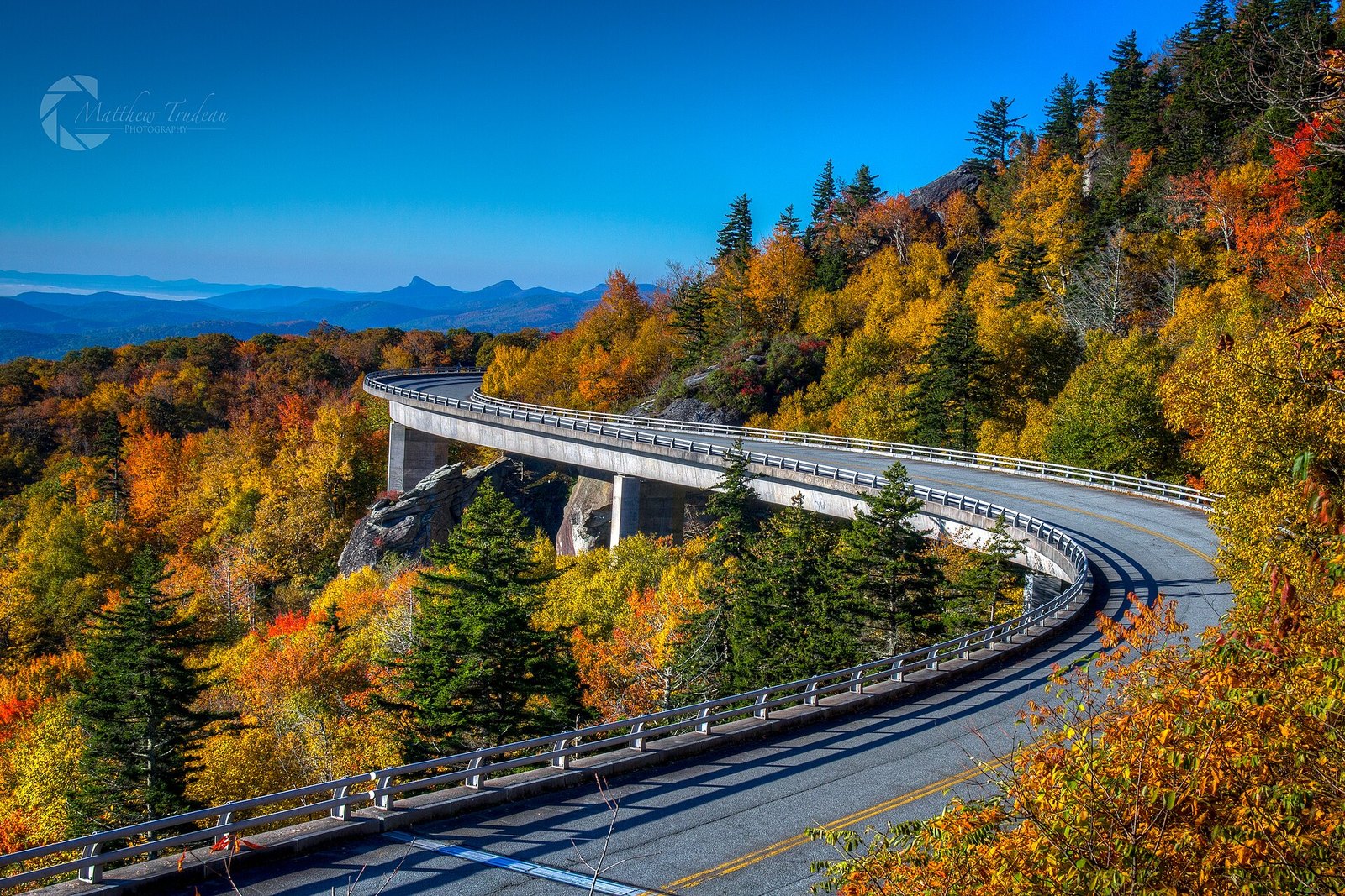 The Linn Cove Viaduct curving along a mountainside of red, orange and yellow trees.