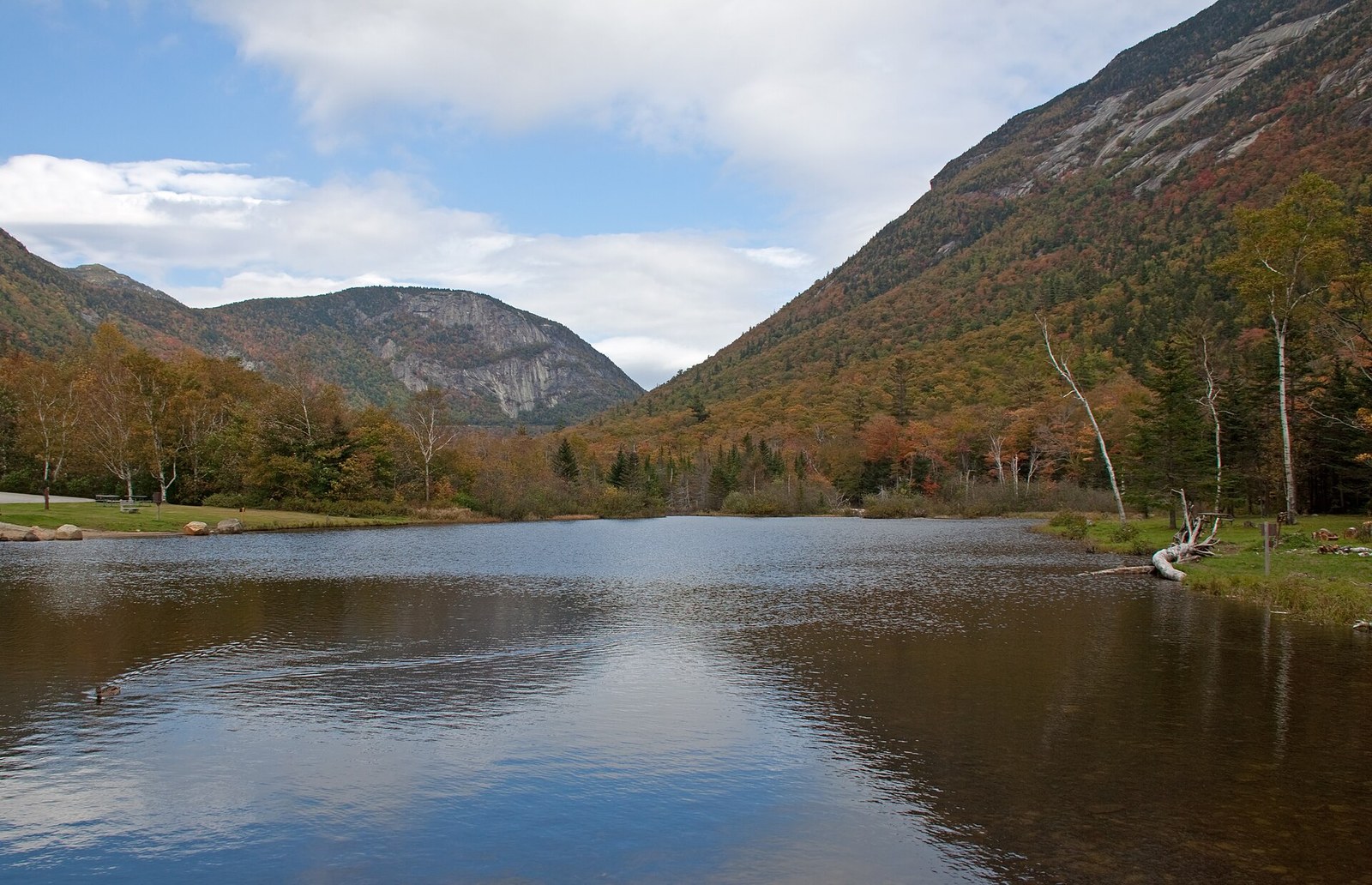 A pond in a steep notch between rock-faced mountains, the slopes in orange and green.