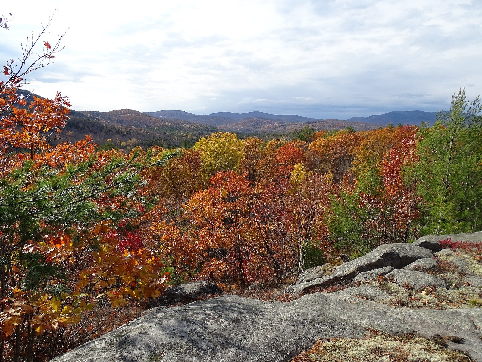 A rock ledge above a hillside of red, orange and yellow trees, with blue ridges beyond.