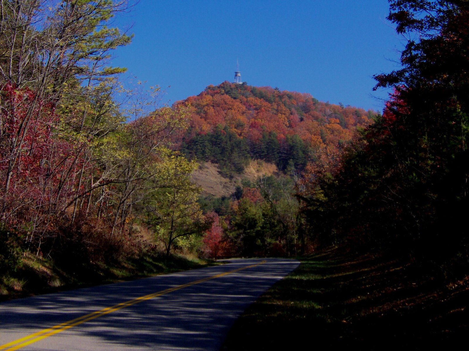 The Foothills Parkway curving toward a ridge of red and orange trees crowned by an observation tower.