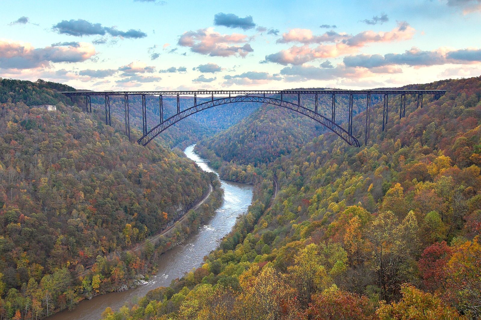 The New River Gorge Bridge arching over the river, with the gorge walls in red, orange and gold.